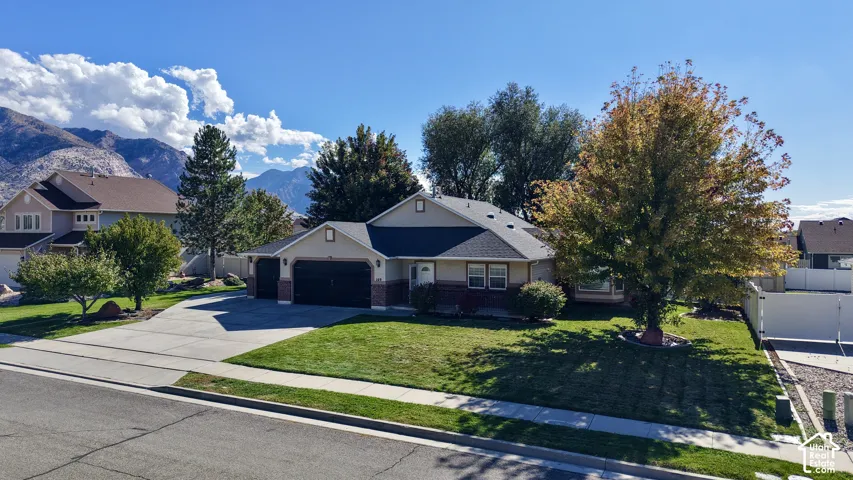 Single-story residence featuring a brick and siding exterior, attached three-car garage, concrete driveway, and expansive lawn under a mountain backdrop