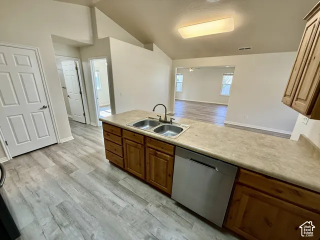Kitchen featuring wood-finish cabinetry, neutral solid-surface countertops, dual-basin stainless steel sink with high-arc faucet, stainless steel dishwasher, and vaulted ceilings