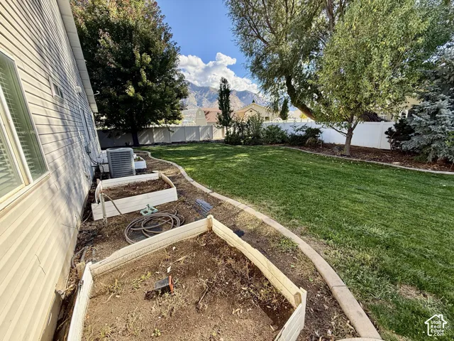Spacious backyard featuring a manicured lawn, mature shade trees, and raised garden beds with wood-finish frames