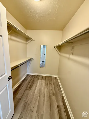 Walk-in closet featuring wood-finish flooring, dual-level white shelving, and a wall-mounted mirror