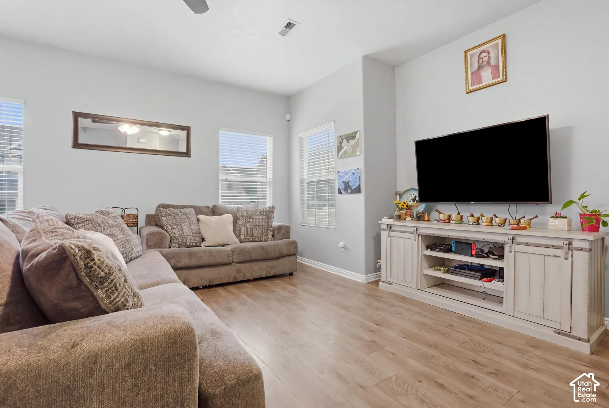 Living space featuring wood-finish flooring, high ceilings, multiple windows with horizontal blinds, and a neutral wall color palette