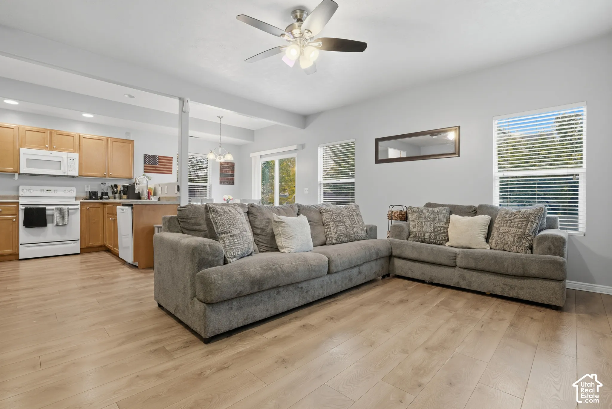 Open concept floor plan with wood-finish flooring, recessed lighting, ceiling fan with integrated light fixture, and multiple windows with blinds