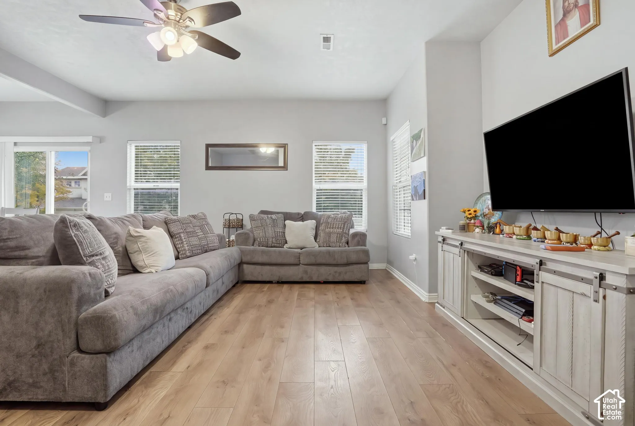Living area featuring wood-finish flooring, recessed ceiling lighting, a multi-blade ceiling fan with integrated light fixture, and multiple windows providing natural light