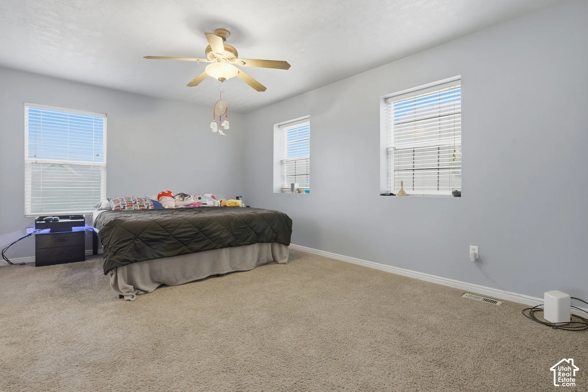 Spacious room featuring neutral carpeting, triple-window configuration, and a central ceiling fan with integrated lighting