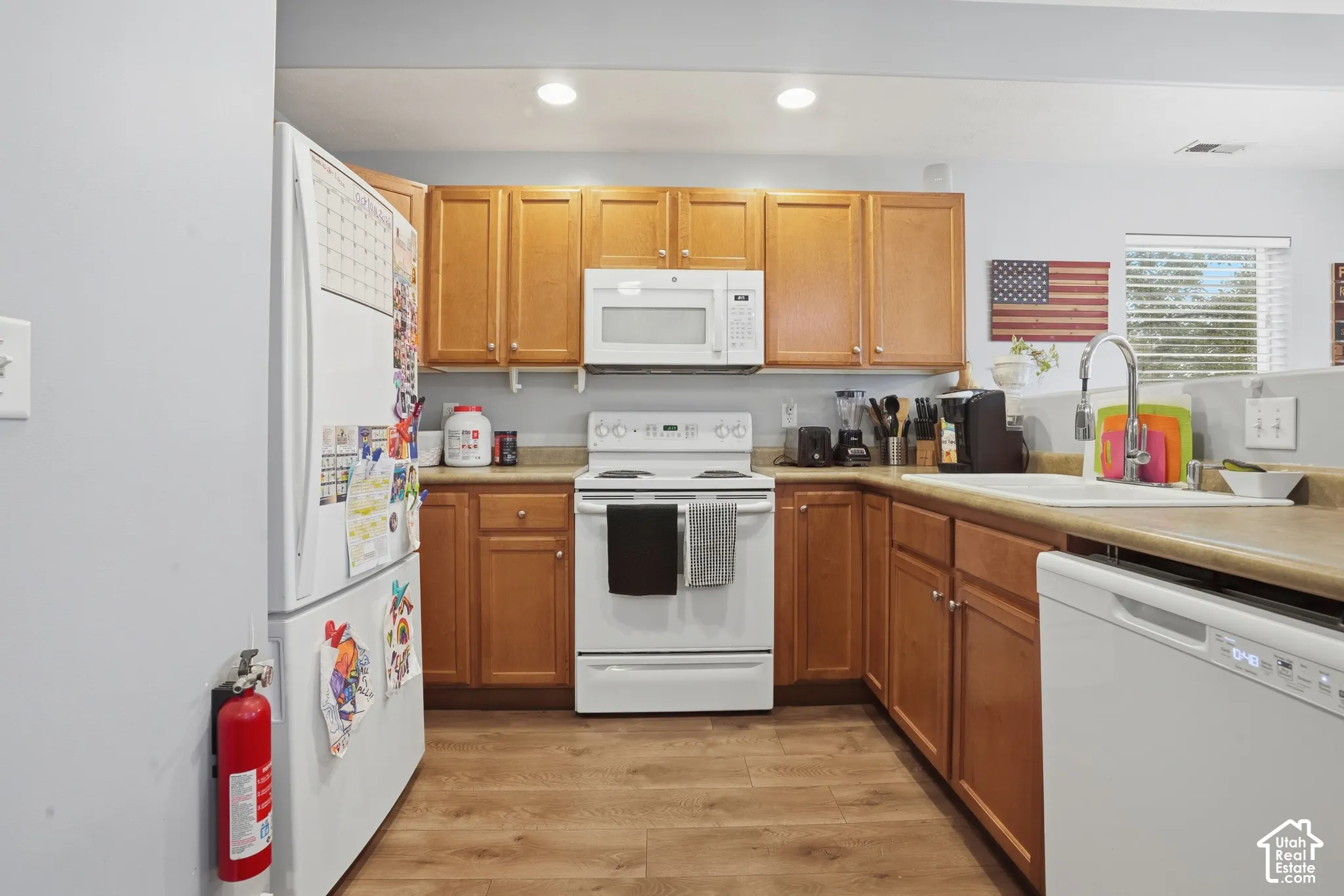 Kitchen featuring natural wood cabinetry, wood-finish flooring, white appliances, and a double-basin sink with a gooseneck faucet