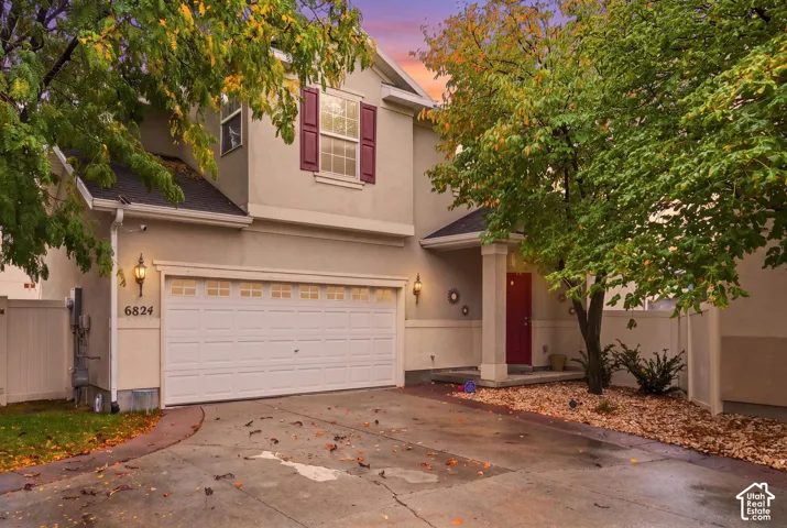 Two-story exterior featuring a stucco facade, attached two-car garage, contrasting window shutters, and a covered front porch entryway