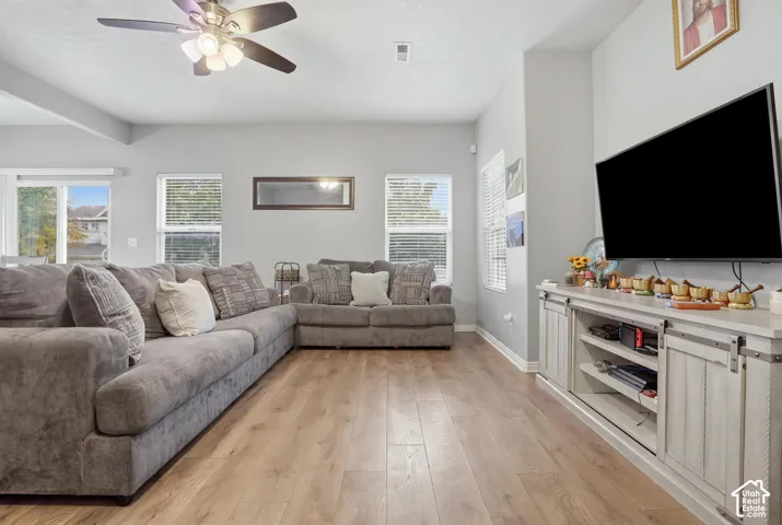 Living area featuring wood-finish flooring, recessed ceiling lighting, a multi-blade ceiling fan with integrated light fixture, and multiple windows providing natural light