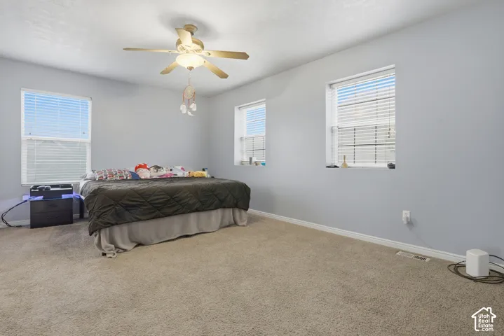 Spacious room featuring neutral carpeting, triple-window configuration, and a central ceiling fan with integrated lighting