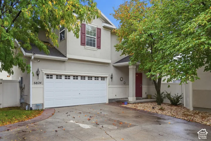 Two-story exterior featuring a stucco facade, a two-car garage with a paneled door, decorative window shutters, and a covered front entryway with a column support