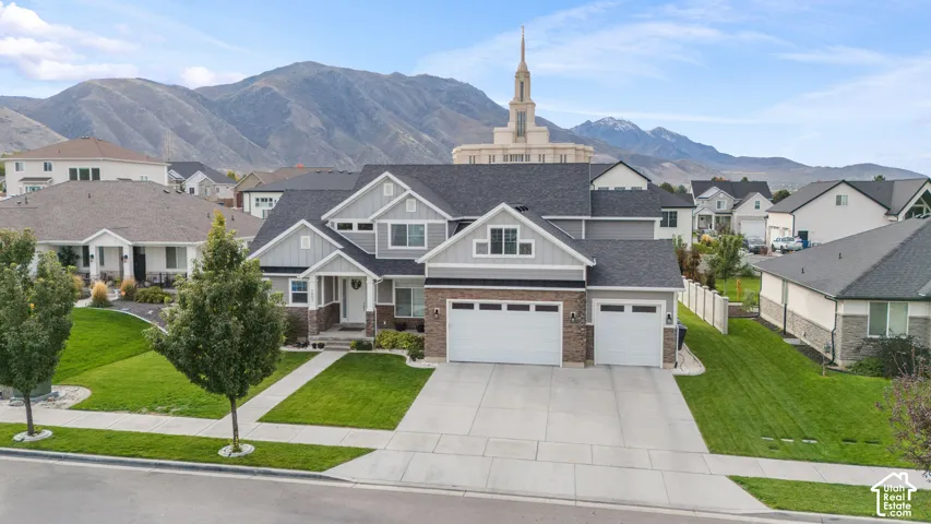 Exterior featuring multi-textured siding, stone veneer accents, a three-car garage, and a concrete driveway set against a mountain backdrop