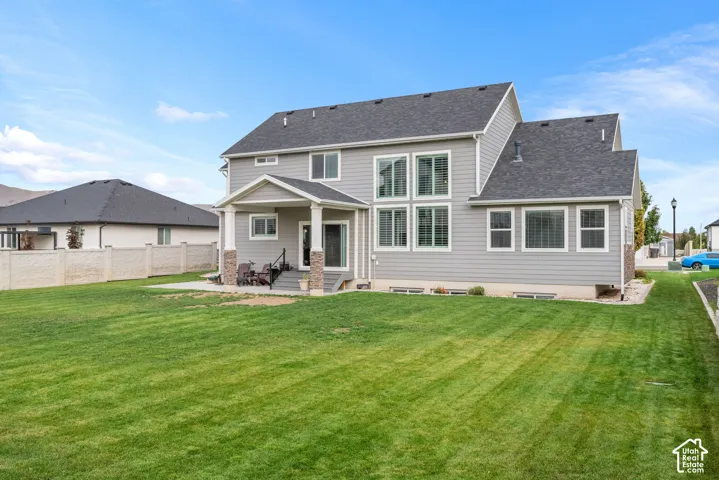 Exterior siding, covered rear patio, stone masonry accents, multi-pane windows, and expansive lawn