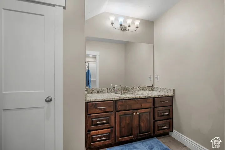 Stained wood vanity with stone-finish countertop, undermount sink, expansive wall-mounted mirror, and multi-bulb vanity light fixture
