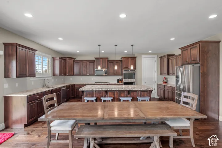 Kitchen featuring stained wood cabinetry, stone countertops, central island, stainless steel built-in appliances, and recessed lighting