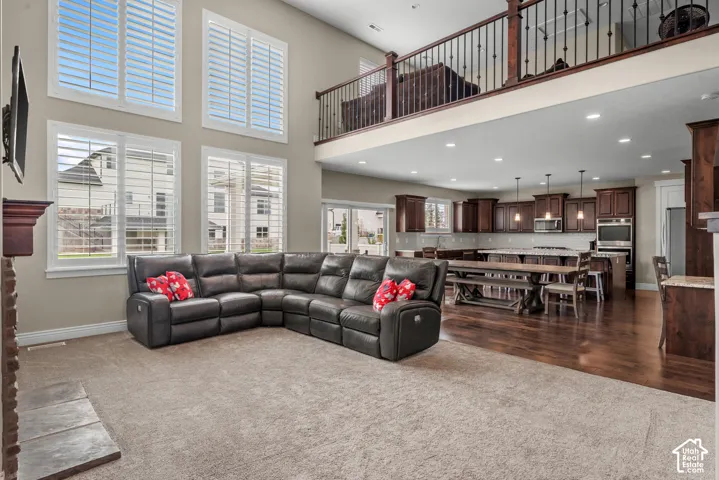 Double-height living area featuring floor-to-ceiling windows with plantation shutters, wood-finish flooring, recessed lighting, and a mezzanine with a dark wood and metal railing
