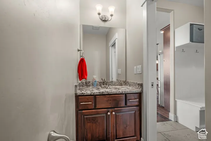 Stained wood vanity with stone-patterned countertop, undermount sink, dual-bulb wall-mounted lighting fixture, and built-in white cabinetry with integrated coat hooks