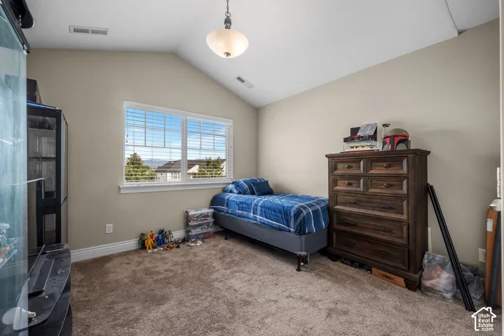 Vaulted ceiling with a central pendant light fixture, large window with blinds, and neutral wall tones
