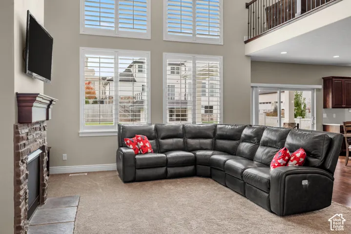 Double-height living area featuring a stone-faced fireplace with a decorative mantle, oversized windows with plantation shutters, and a second-level balcony with metal railing