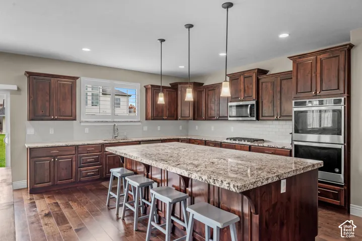 Kitchen featuring stained wood cabinetry, stone countertops, a large center island, stainless steel double wall ovens, and wood-finish flooring