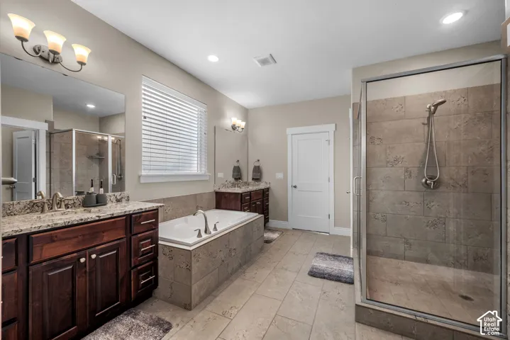 Bathroom featuring dark wood cabinetry, stone-finish countertops, a soaking tub with stone tile surround, and a walk-in shower with a handheld fixture
