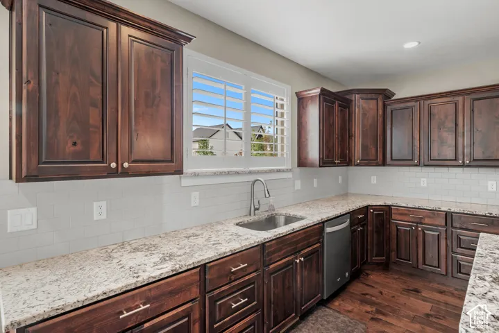 Kitchen featuring stained wood cabinetry, light-toned stone countertops, subway tile backsplash, stainless steel under-mount sink with pull-down faucet, and wood-finish flooring