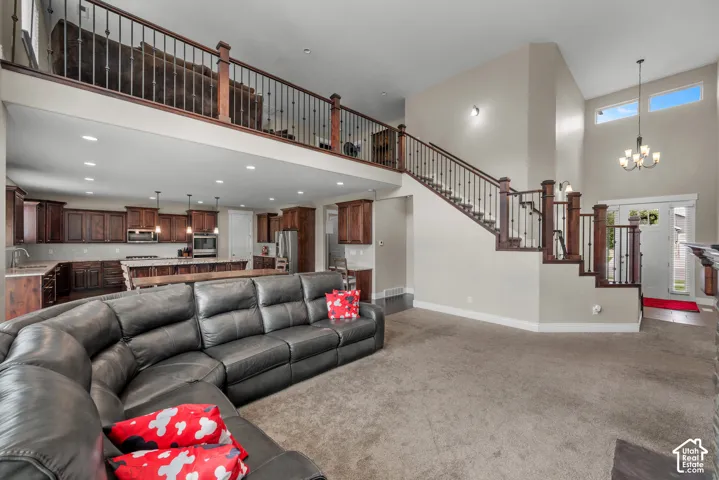 Open-concept space featuring vaulted ceilings, a prominent wooden staircase with metal balusters, dark wood cabinetry, recessed lighting, and a multi-tiered chandelier