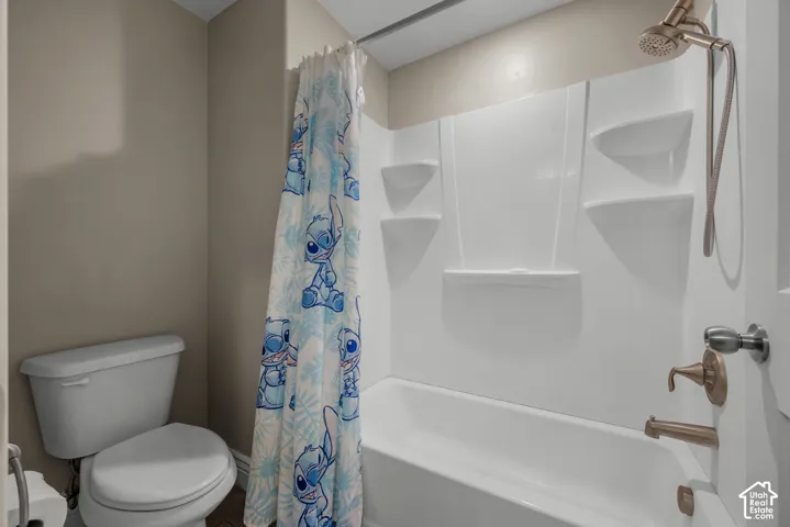 Bathroom featuring a white bathtub and shower surround with integrated shelving, metallic finish plumbing fixtures, and a white toilet