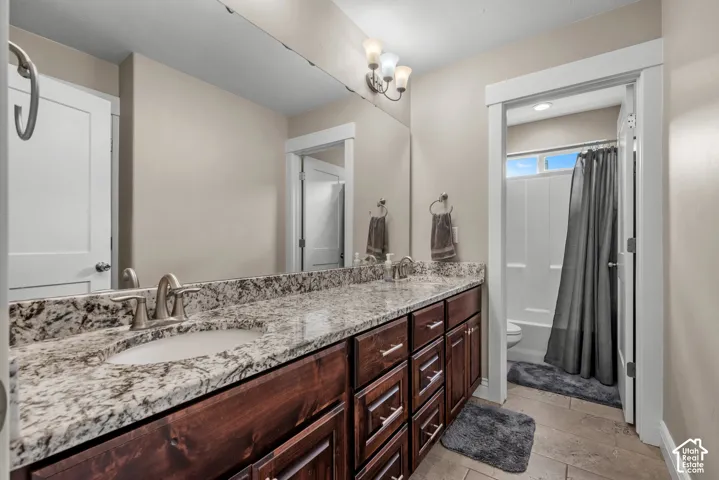 Double vanity with stone-finish countertop and under-mount sinks, wood-finish cabinetry, full-width vanity mirror, and three-light fixture