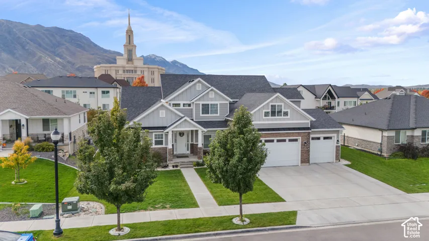 Two-story residence featuring composite shingle roofing, vertical and horizontal siding, stone veneer accents, and an attached three-car garage, set against a mountain backdrop