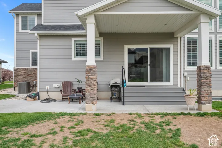 Covered patio featuring stone-pillar supports, horizontal siding, concrete flooring, and a set of stairs leading to a sliding glass door