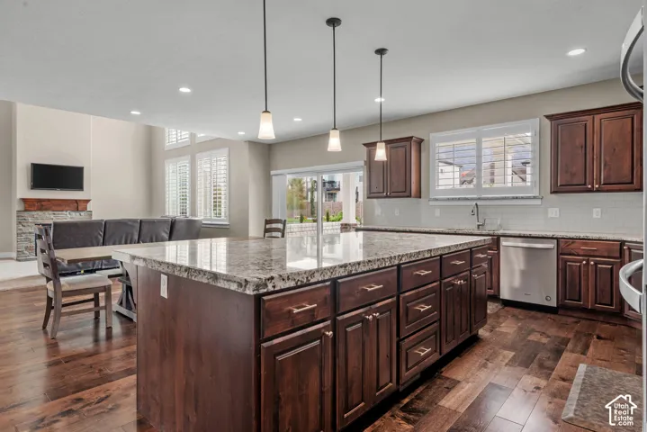 Kitchen featuring a large central island with stone-finish countertops, dark wood-finish cabinetry, stainless steel dishwasher, recessed lighting, and wood-finish flooring