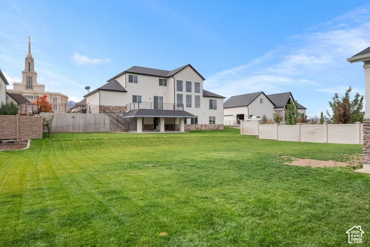Expansive rear yard featuring a manicured lawn, a concrete patio, an elevated metal-railed deck, and perimeter fencing