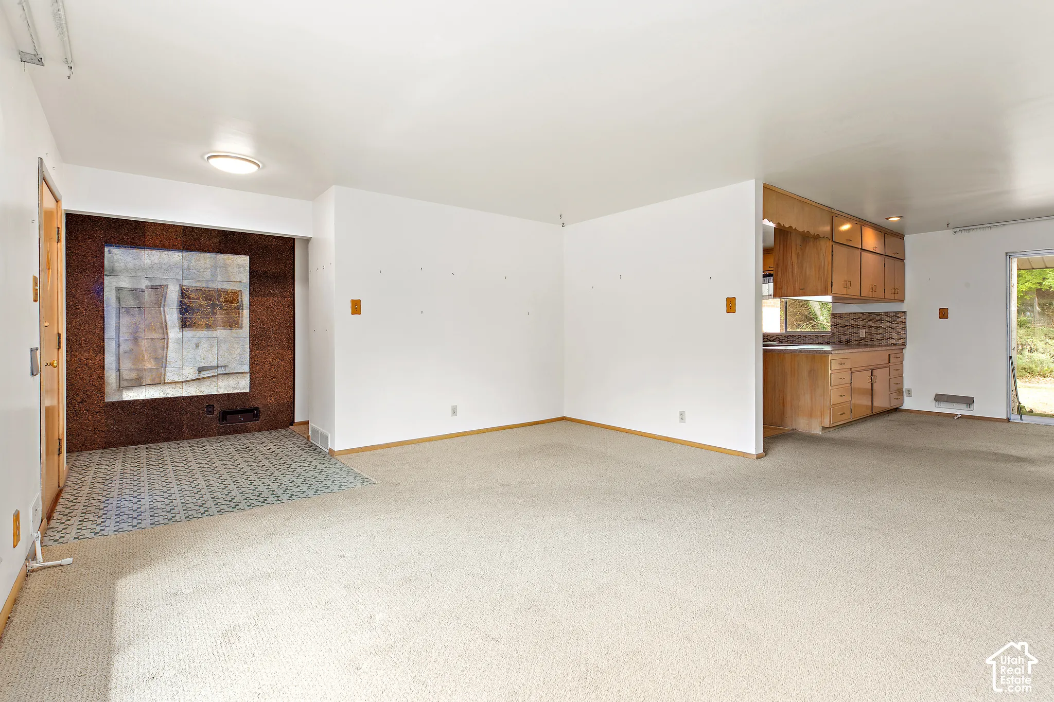 Open-concept interior featuring wall-to-wall carpeting, a decorative stone-finish accent wall with tile hearth, and wood-finish cabinetry in the kitchen area