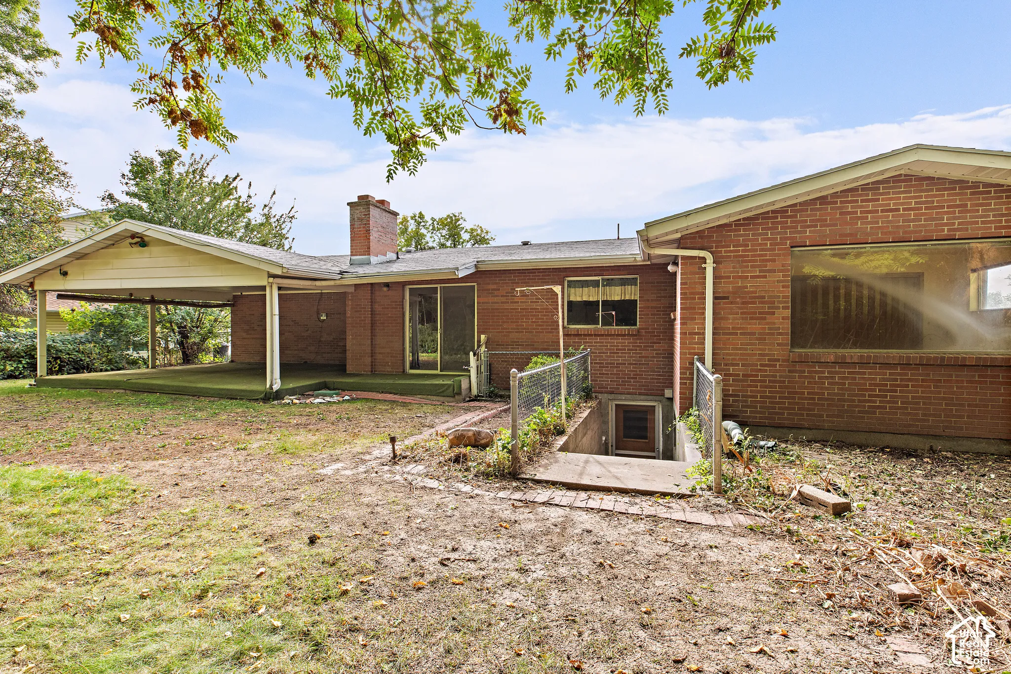 Brick exterior featuring a covered patio, exterior brick chimney, sliding glass door, and recessed basement entrance