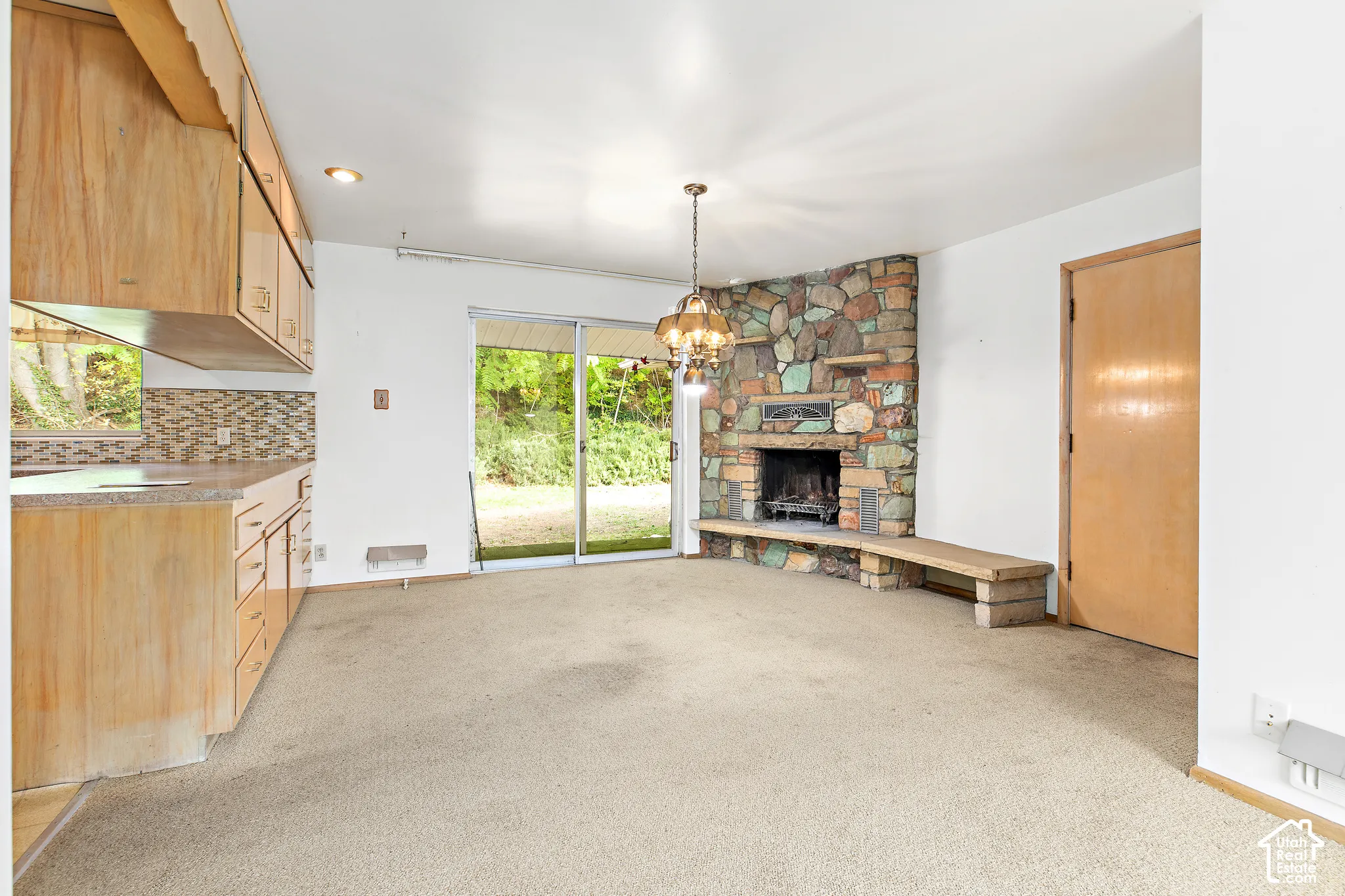 Corner fireplace featuring multi-colored stone masonry and a concrete hearth, sliding glass door, wooden cabinetry, and hanging chandelier