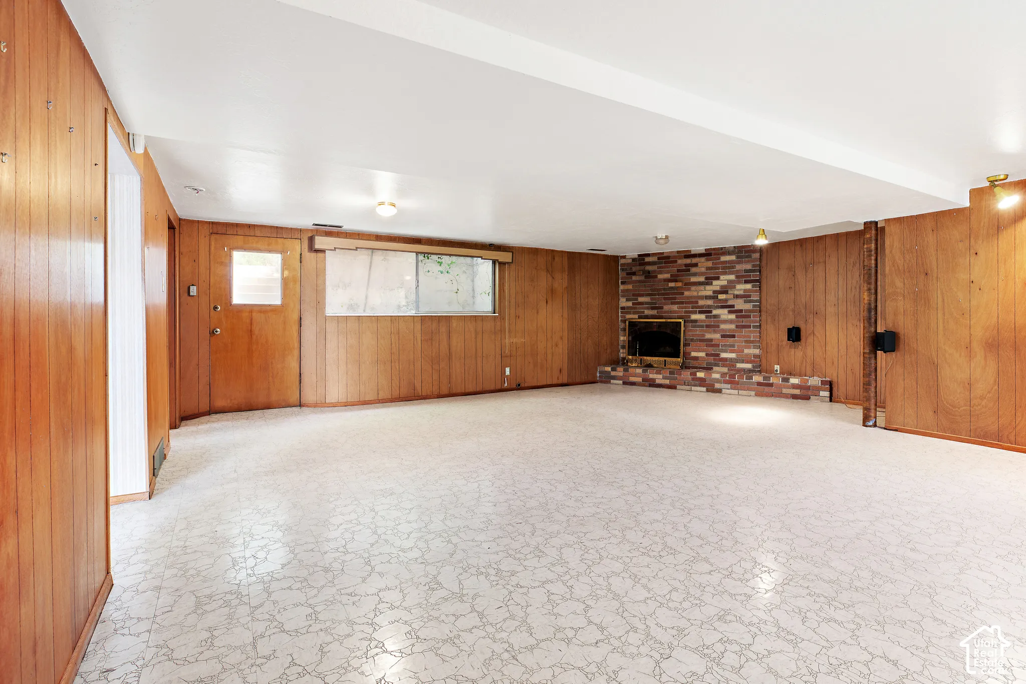 Interior space featuring wood paneling, a full-height brick fireplace, a neutral patterned floor, and an exterior door
