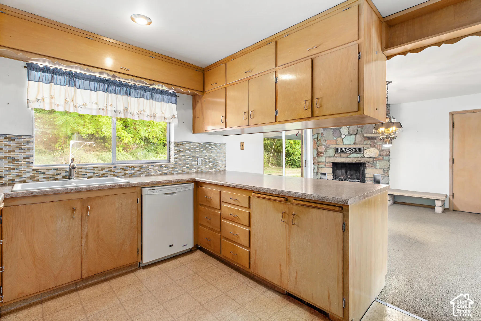 Kitchen featuring wood cabinetry, integrated dishwasher, mosaic tile backsplash, and stone-surround fireplace