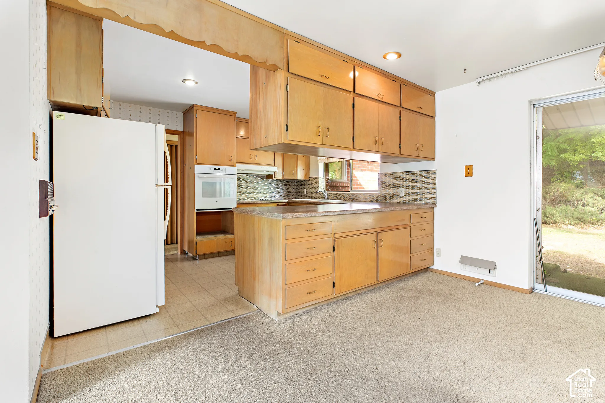 Kitchen featuring light wood cabinetry, stone-patterned laminate countertops, mosaic tile backsplash, built-in wall oven, and sliding glass door