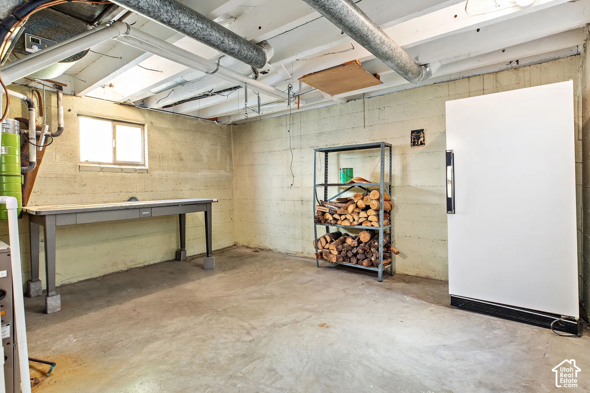 Utility area featuring painted concrete block walls, exposed ceiling joists, concrete flooring, and a single-pane window
