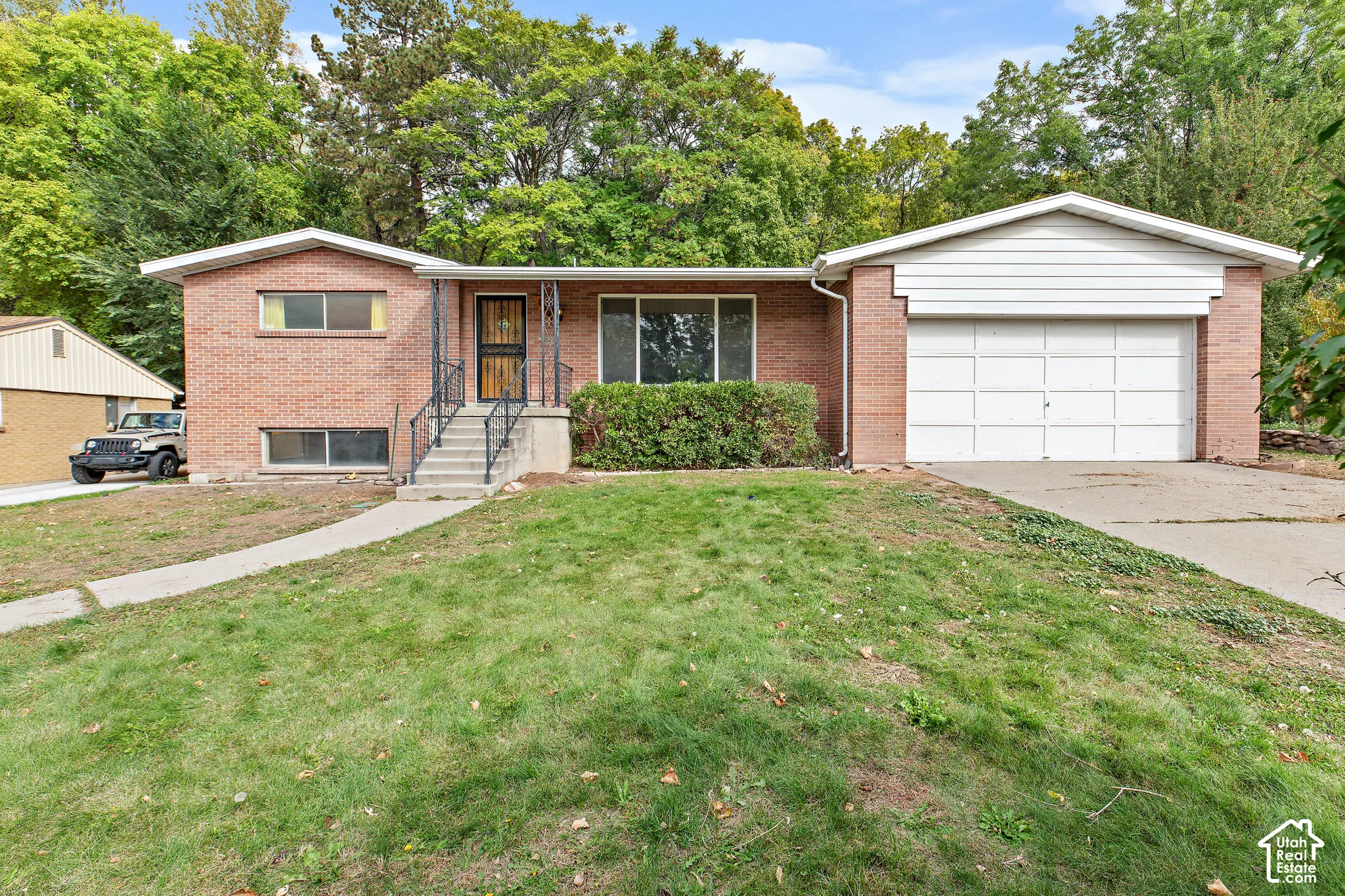 Single-story brick exterior featuring a multi-paneled garage door, concrete front staircase, iron handrails, and a concrete driveway