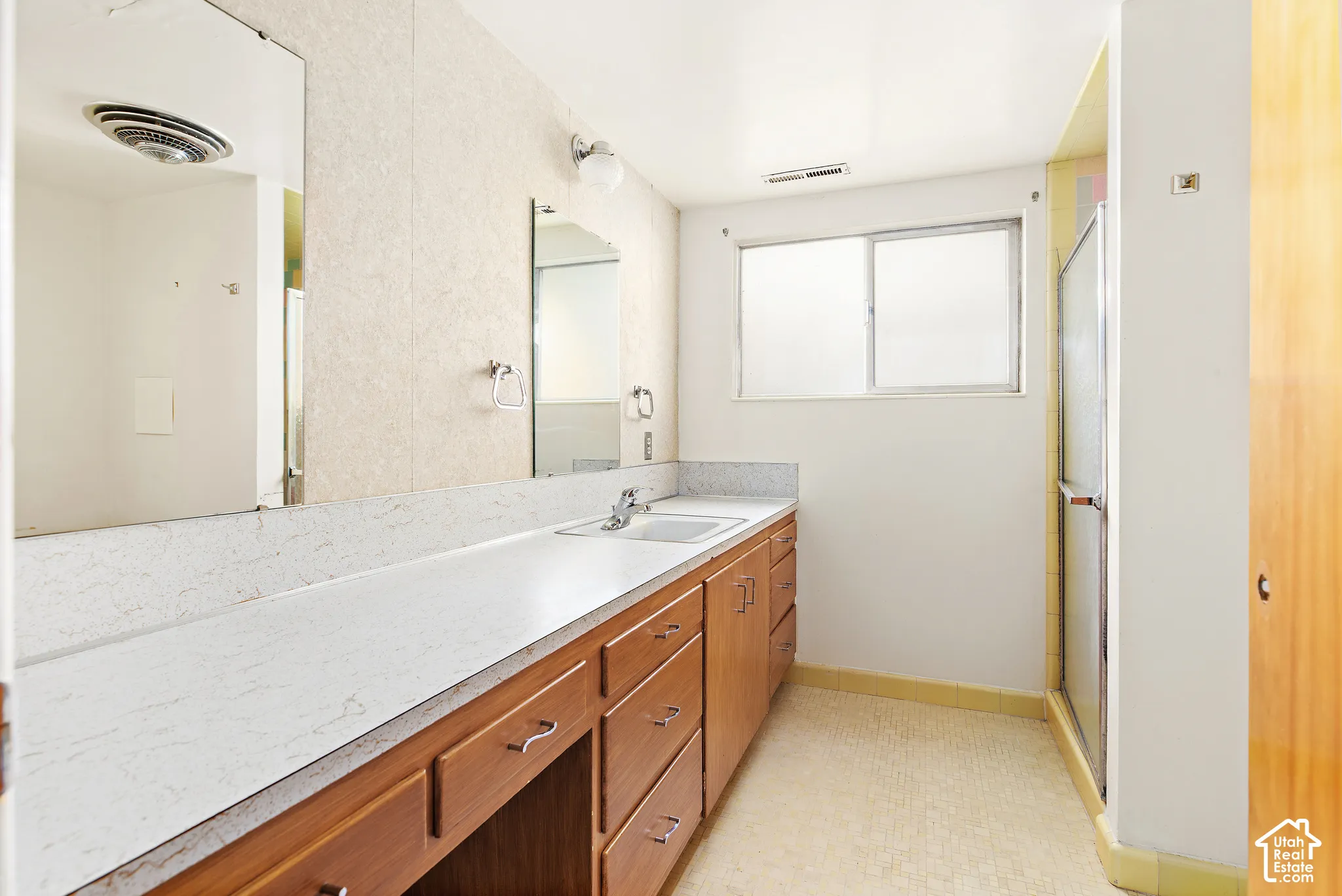 Full-width vanity with countertop basin, wood-finish cabinetry, wall-mounted mirror, and glass-enclosed shower