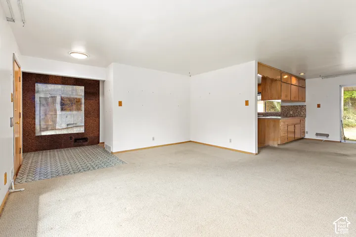 Open-concept interior featuring wall-to-wall carpeting, a decorative stone-finish accent wall with tile hearth, and wood-finish cabinetry in the kitchen area