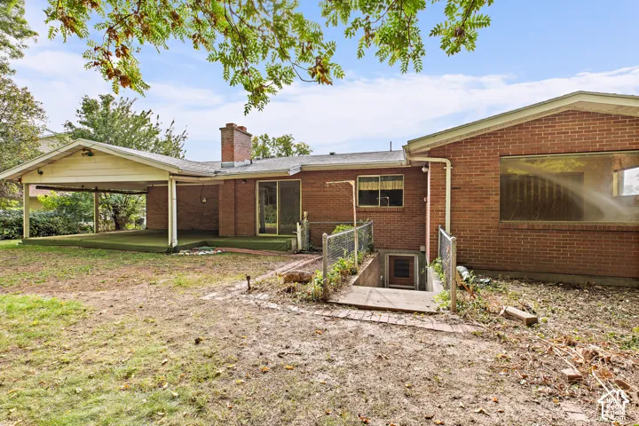 Brick exterior featuring a covered patio, exterior brick chimney, sliding glass door, and recessed basement entrance