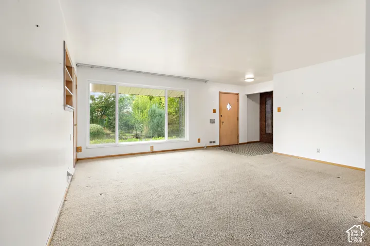 Open-concept interior featuring wall-to-wall carpeting, large picture window with exterior scenery, wood-grain entry door, and flush-mount lighting