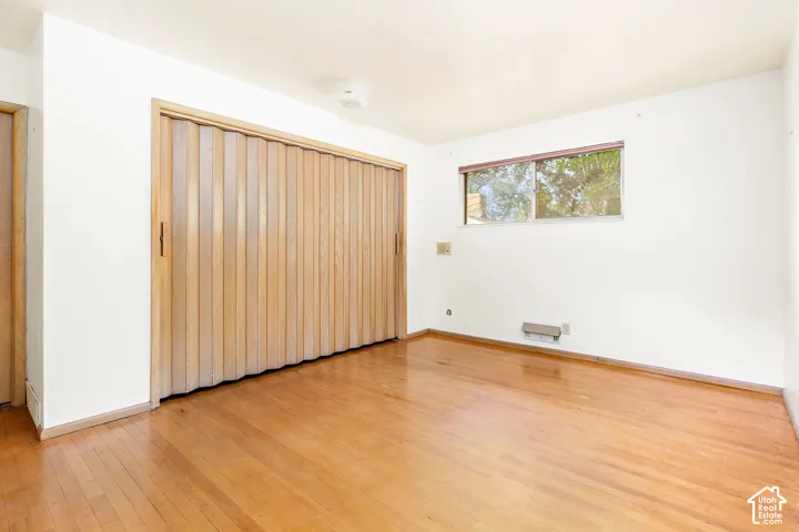 Wood-finish flooring, full-wall accordion-style closet doors, and natural lighting provided by a sliding window