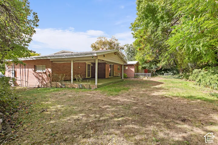 Red brick exterior featuring a covered patio, gabled roofline, and expansive grounds with mature trees