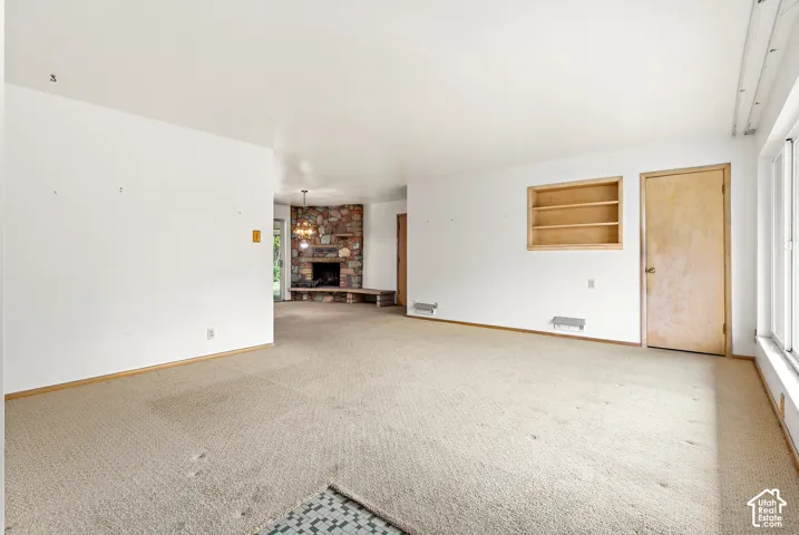 Interior space featuring a corner stone fireplace with a raised stone hearth, built-in wooden shelving, and wall-to-wall carpeting