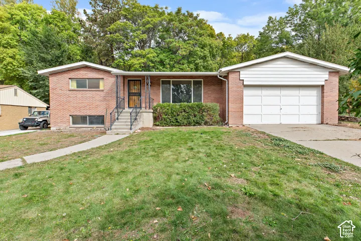 Single-story brick exterior featuring a multi-paneled garage door, concrete front staircase, iron handrails, and a concrete driveway