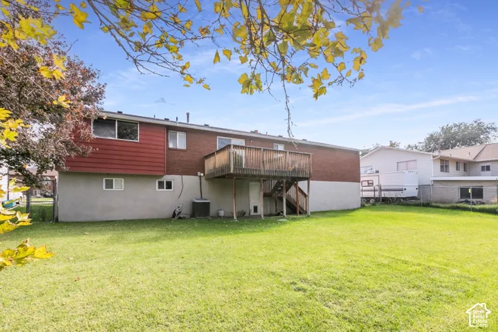 Backyard featuring a sprawling lawn, raised wood deck with staircase, brick and stucco exterior, and chain-link perimeter fencing.