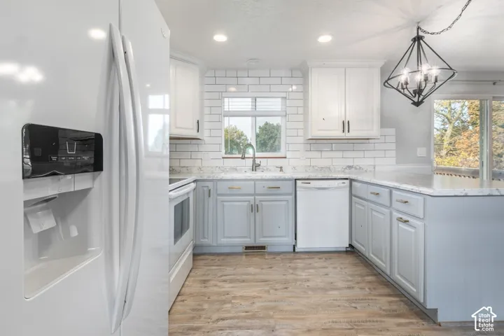 Kitchen featuring light gray and white cabinetry, stone-patterned countertops, white subway tile backsplash, wood-finish flooring, and a geometric metal pendant light fixture.