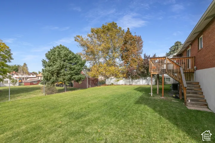 Expansive backyard featuring a manicured lawn, raised wood deck with staircase, mature trees, and perimeter fencing.